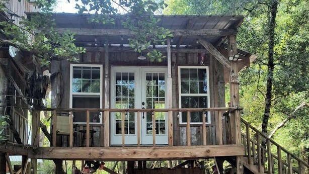A wooden cabin with a covered deck, a staircase, and a small outdoor seating area.