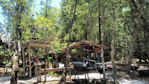 Ein rustikaler Außenbereich mit einer Holzhütte, einem Grill und verschiedenen Küchengeräten.