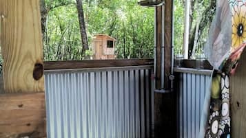 Une terrasse en bois avec une rambarde en métal, une petite structure en bois en arrière-plan et un rideau coloré.