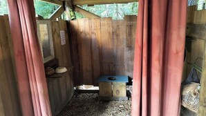 A wooden structure with a blue toilet, a shelf with a bowl, and a hanging lantern.