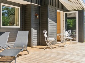 Eine überdachte Terrasse im Freien mit Metallstühlen und einem Tisch, eine Holzterrasse und eine Glastür zum Garten.