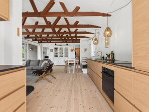 A modern kitchen with wooden cabinets, a black countertop, and a dining area with a table and chairs. - "Antonie" - 350m from the sea by Interhome (Vejby)
