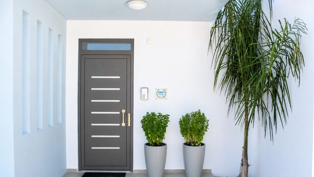 A modern entrance with a grey door, potted plants, and a wall-mounted sign. - Zidros Apartments Ground Floor Apartment 2 (Sfakaki)