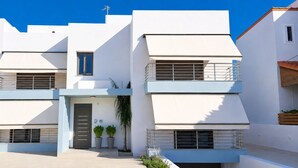 A modern two-story residential building with a flat roof, large windows, and a balcony with a metal railing. - Zidros Apartments Ground Floor Apartment 2 (Sfakaki)