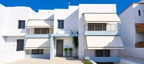 Ein modernes Wohngebäude mit zwei Stockwerken, flachem Dach, großen Fenstern und einem Balkon mit Metallgeländer.