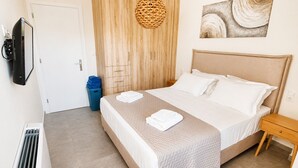 A hotel room with a bed, a bedside table, a wall-mounted TV, a wooden wardrobe, and a blue trash bin. - Zidros Apartments Ground Floor Apartment 2 (Sfakaki)