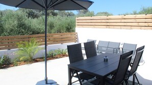 An outdoor patio with a table and chairs, an umbrella, and a wooden fence. - Zidros Apartments Ground Floor Apartment 2 (Sfakaki)