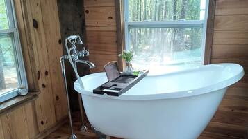 A clawfoot bathtub in a wooden cabin with a window overlooking a forest.