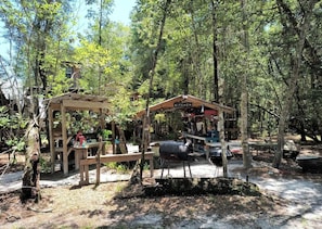 A rustic outdoor kitchen area with a wooden structure, a barbecue grill, and a dining table. - Off-Grid Cabin Retreat Near Satilla River, Georgia (WAYNESVILLE)