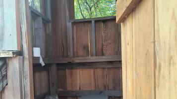 A wooden cabin with a window, a metal trash can, and a bucket.