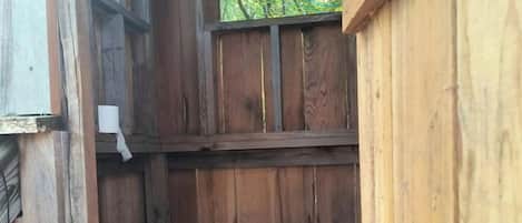 A wooden cabin with a window, a metal trash can, and a bucket.