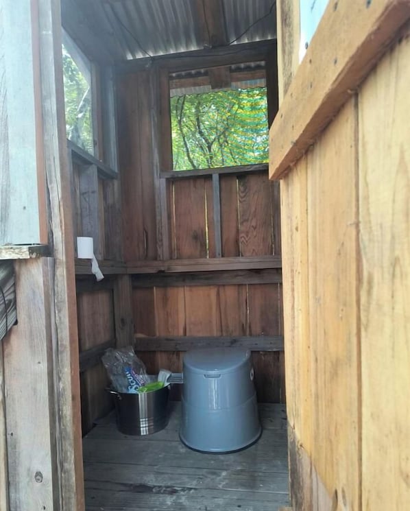 Una cabaña de madera con una ventana, un bote de basura metálico y un balde.