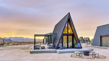 A modern, triangular-shaped building with a glass facade, outdoor seating area, and a desert landscape in the background.