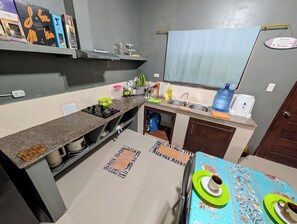Cocina compacta con estufa a gas, lavamanos y una pequeña zona de comedor con mesa.