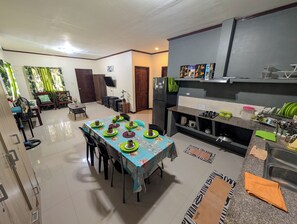 Un comedor con una mesa preparada para cuatro, una cocina con electrodomésticos modernos y una sala de estar con sofá y televisor.