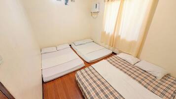 Une chambre avec deux lits, un plancher en bois, un climatiseur fixé au mur et une fenêtre avec des rideaux.