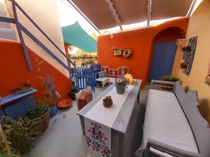 Un espacio comedor al aire libre cubierto, con mesa, sillas y plantas en macetas.