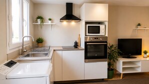 A modern kitchen with a built-in microwave, oven, and dishwasher, a TV on a stand, and a window providing natural light. - Charming 1-bedroom apartment near Geneva, between the lake and the mountains (Bons-en-Chablais)