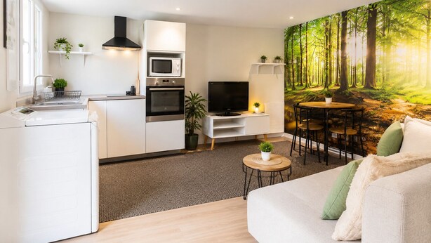 A modern living room with a sofa, a dining table, and a kitchen area with appliances. - Charming 1-bedroom apartment near Geneva, between the lake and the mountains (Bons-en-Chablais)