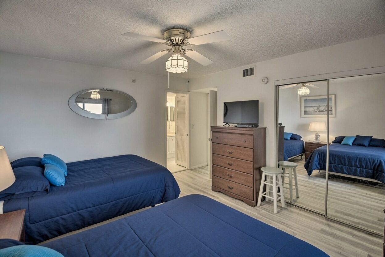 A bedroom with two beds, a dresser, a TV, and a ceiling fan.
