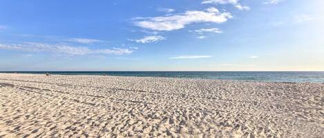 A wide sandy beach with a clear sky and calm sea.