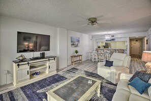 A living room with a flat-screen TV, a coffee table, and a sofa. There is a dining area with chairs and a table in the background. - Cozy 2-bedroom condo with AC in terrific Daytona Beach Shores (Daytona Beach Shores)