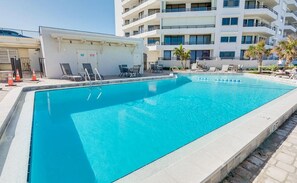 Una piscina rettangolare con superficie d'acqua blu trasparente, circondata da sedie a sdraio e un piccolo edificio con una porta e finestre.