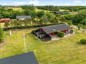 Eine rote Holzhütte mit einer Veranda, umgeben von einem grünen Rasen und Bäumen.