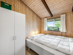 Une chambre avec un plafond en bois, un lit avec une literie blanche, une fenêtre avec des rideaux et un panier de rangement vert.