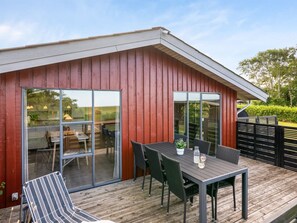Un espace extérieur abrité, doté d’une table et de chaises, une porte vitrée donnant sur un espace intérieur et une terrasse en bois.