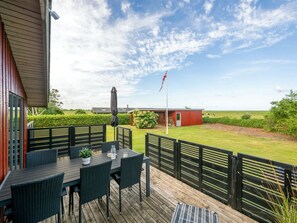 Una terraza con asientos al aire libre, una bandera y una vista de una granja al fondo.