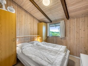 Un dormitorio con cama, paredes de madera, una ventana con vistas y un ventilador de techo.