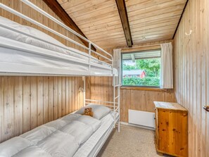 Ein Schlafsaal mit Etagenbetten und Blick aus dem Fenster auf ein rotes Haus und Grünpflanzen.