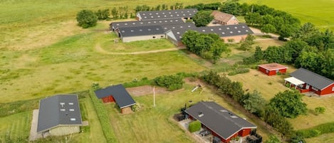 A rural property with multiple buildings, including barns and residential structures, surrounded by expansive green fields and a clear sky.
