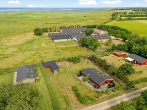 Propiedad rural con varias construcciones, incluyendo establos y viviendas, rodeada de amplios campos verdes y un cielo despejado.