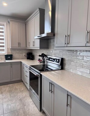 A kitchen with grey cabinets, a stainless steel stove, and a tiled backsplash. - Sleeps 16 and more | Bedrooms with ensuite washrooms (Springwater)