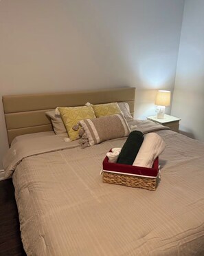 A neatly made bed with a beige headboard, a bedside lamp, and a basket with folded towels. - Sleeps 16 and more | Bedrooms with ensuite washrooms (Springwater)
