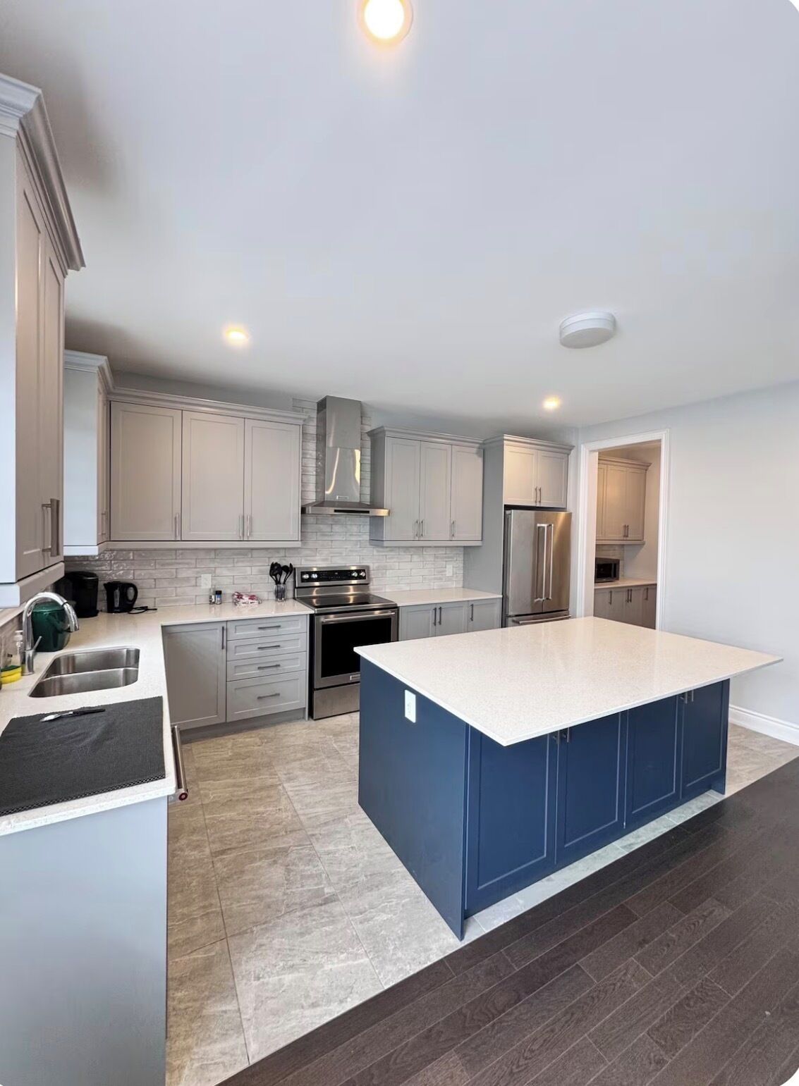 A modern kitchen with white cabinets, a central island, stainless steel appliances, and a dark wood floor.
