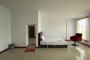 Quarto de hotel com uma cama, uma cadeira vermelha, uma janela com cortinas e uma porta que dá para outro quarto.