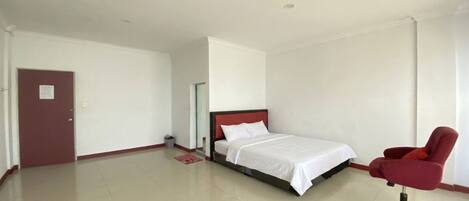 A hotel room with a bed, a red chair, and a door.