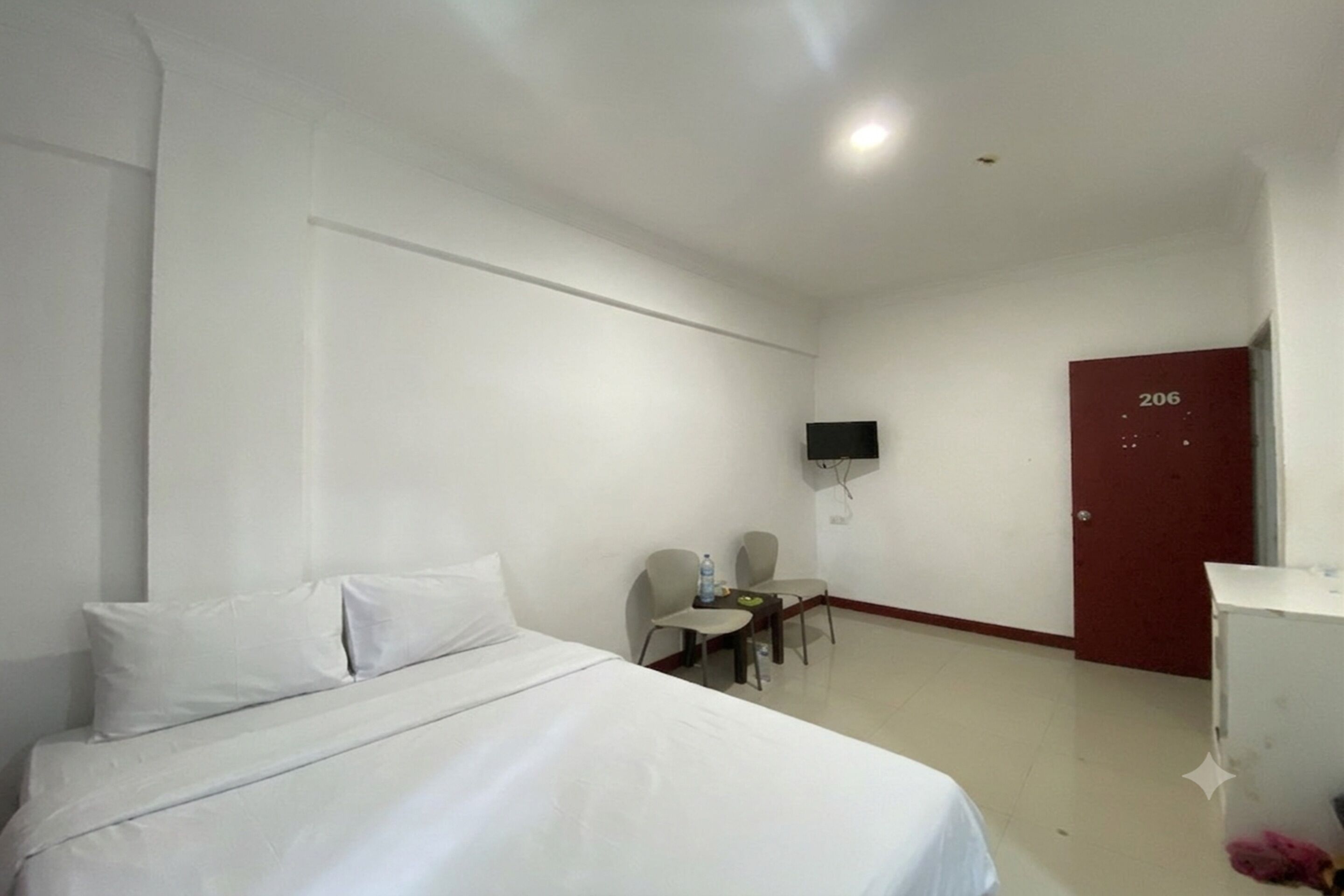 Habitación de hotel con cama, escritorio, silla, televisor montado en la pared y puerta con el número 206.