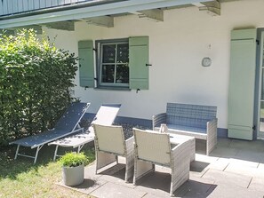 Eine Terrasse mit Gartenmöbeln, einem Blumentopf und einem Fenster mit Fensterläden.