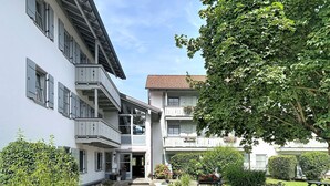 A courtyard with a paved walkway, outdoor seating, and a building with multiple balconies and windows. - Bergzeit by Interhome (Oberaudorf)