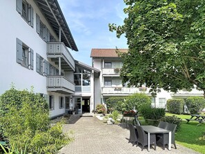 Ein Innenhof mit gepflastertem Weg, Außenbestuhlung und einem Gebäude mit mehreren Balkonen und Fenstern.