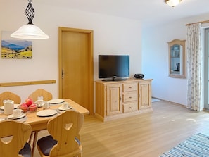Ein Essbereich mit einem Holztisch, gedeckt für vier Personen, einem Fernseher auf einem Schrank und einer Tür zu einem anderen Raum.