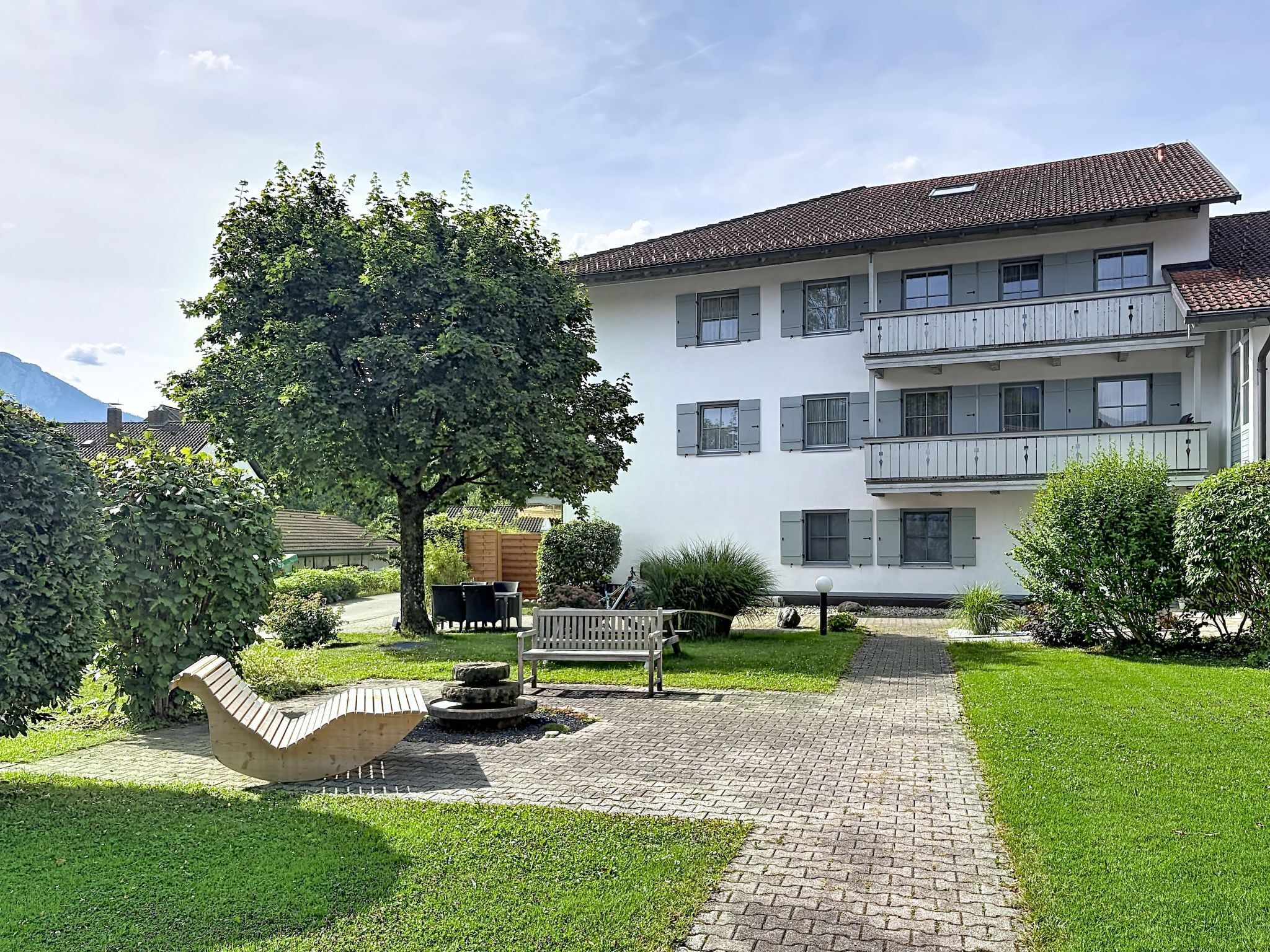 A multi-story building with a paved courtyard, a bench, and a tree.
