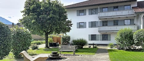 A multi-story building with a paved courtyard, a bench, and a tree.