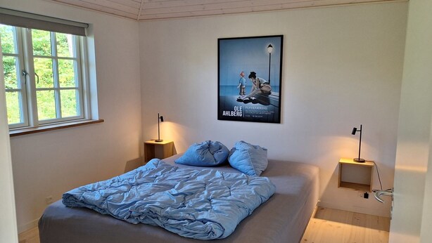 Un dormitorio con una cama, dos mesitas de noche, un cartel en la pared y una ventana.