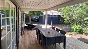 Un patio techado con mesa y sillas, un coche al fondo y un cobertizo.