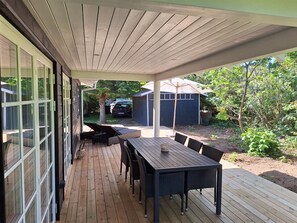 Eine überdachte Terrasse mit Tisch und Stühlen, ein Auto im Hintergrund und ein Schuppen.